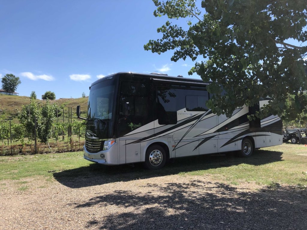 An RV and car sit on a gravel lot in front of a vineyard in South Dakota.